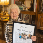 a woman holding a framed story titled 'Kind & Gentle'