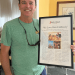 a man holding a framed story titled 'We Love Him Endlessly'