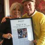 a husband and wife couple holding a framed story titled 'Pidgie & Jay: 55 Years of Love and Family'