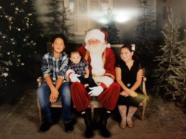 Lilian Wilson's children sitting on a bench with Santa around some Christmas trees