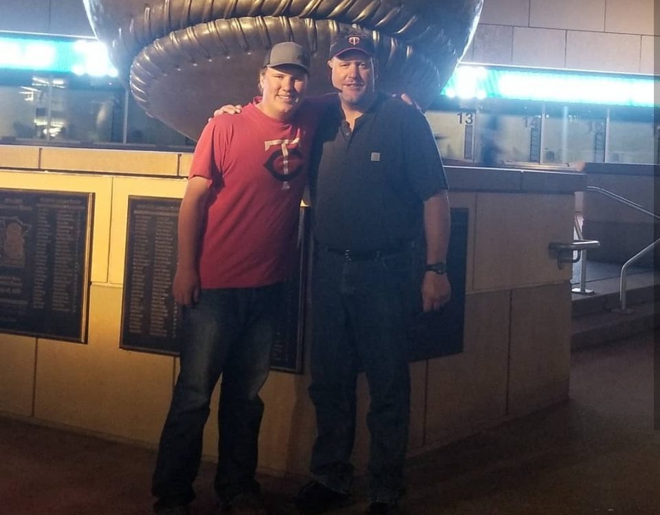 Jim Borkowski and his son outside Target Field in front of the giant baseball statue wearing Twins gear