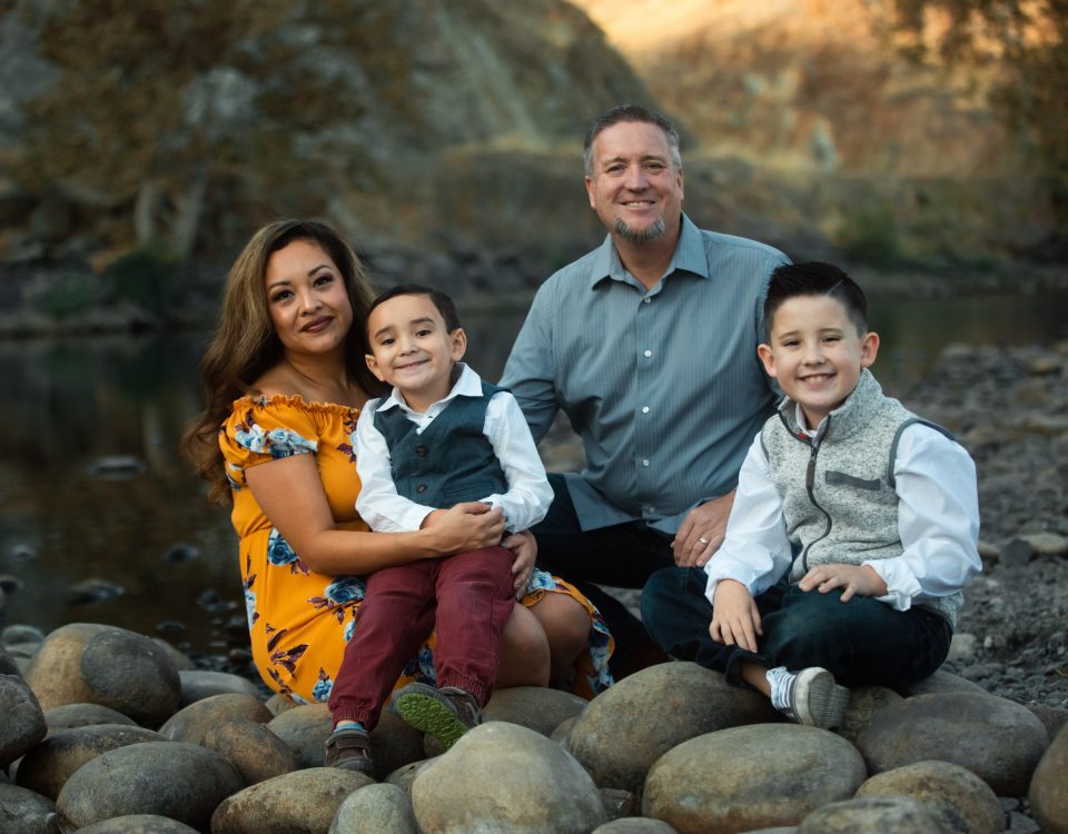 Valarie Melton with her husband and their two young boys sitting on the rocks by the river