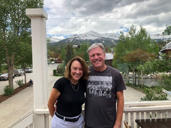 Jeff and Therese smiling on the deck in front of the snowcapped mountains