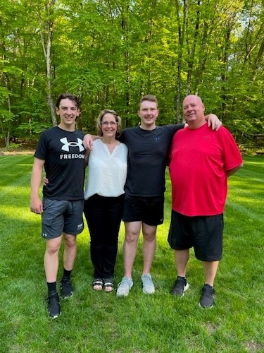 Jenn O’Connor with her family standing outside in the grass in front of the woods