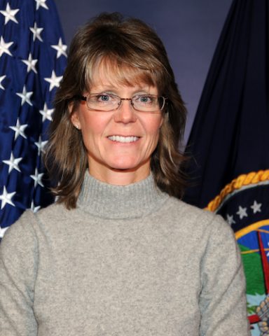 LTC (USAFR Ret) Julie Ziegenhorn standing in front of the two flags she serves