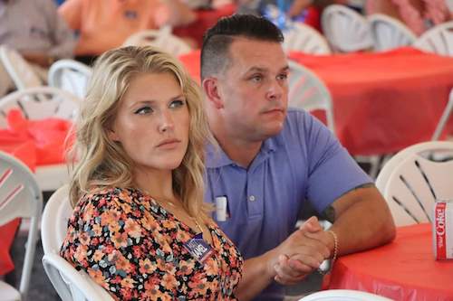 Nikki Pascal and Chris sitting at an event with orange plastic tablecloths