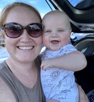 Megan Hutton and Declan smiling in front of the open car trunk