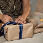 A woman packing a gift with a blue ribbon.