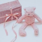 prink yarn crochet teddy bear sitting next to pink gift box