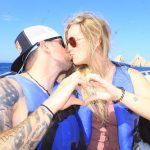 Cody and Amber in vests on a boat making hand hearts